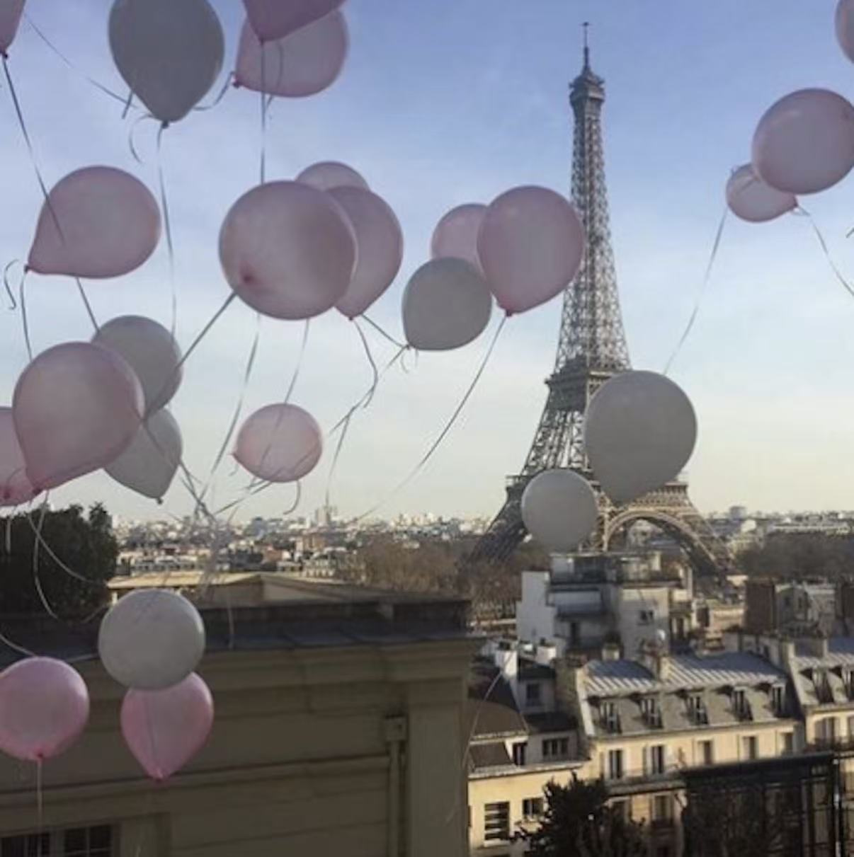 Pink and white balloons are floating near the Eiffel Tower in Paris.